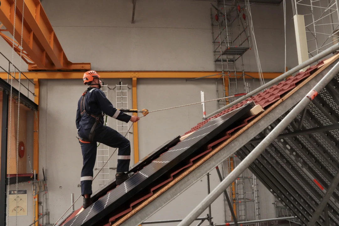 man in loods met helm op en harnas aan lopend op schuin dak
