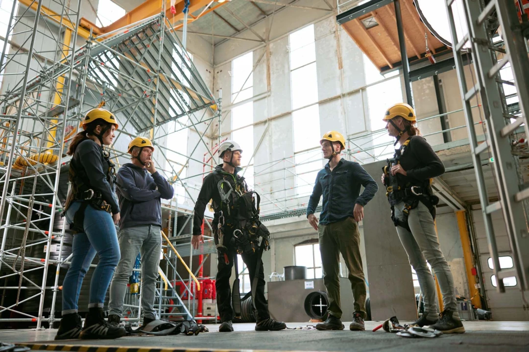 personen in rij in loods met helm en harnas