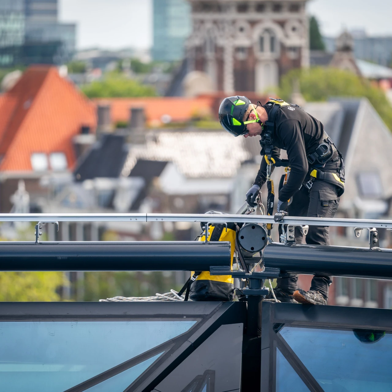 een man die op een dak staat naast een railsysteem, aangelijnd en met een rugzak op zak