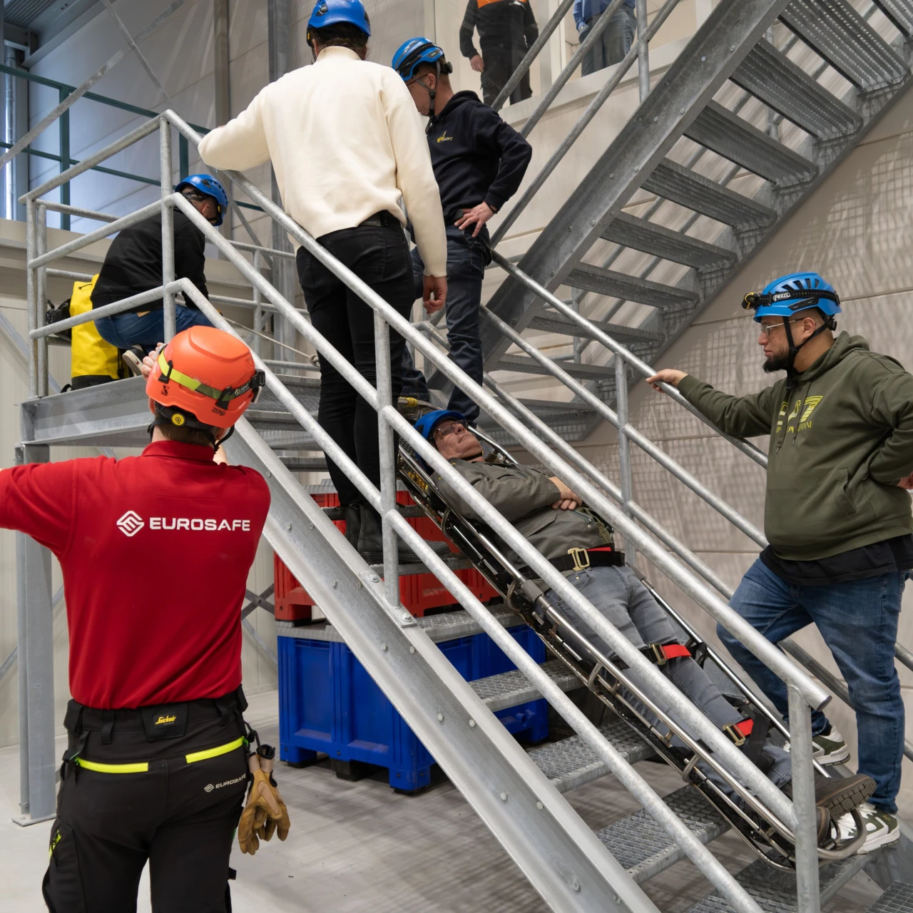 mensen bij trap met helm op die iemand op brancard naar boven brengen