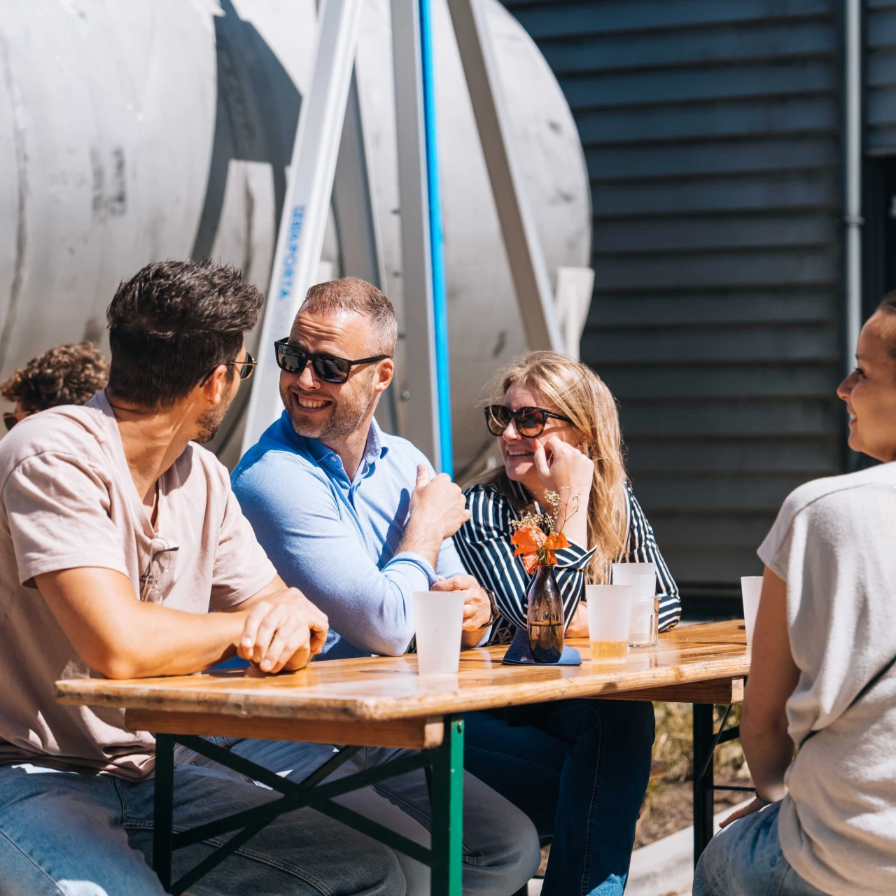 Meerdere personen, zowel man als vrouw, die aan een picnictafel zitten voor een silo