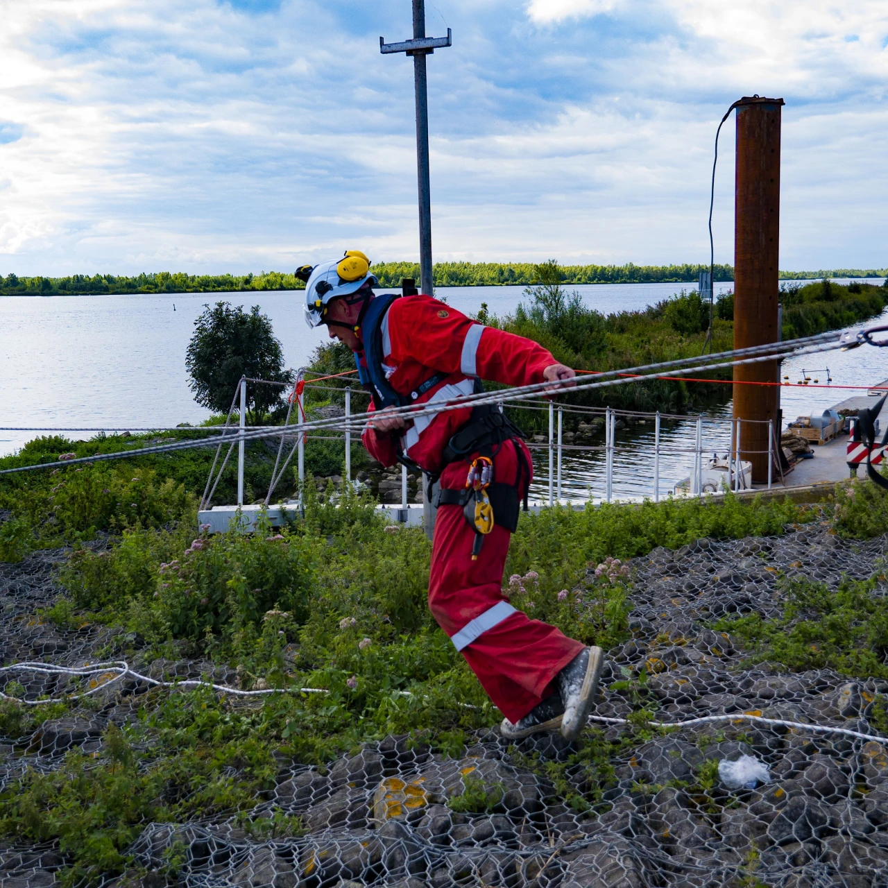 man met helm en reddingsvest bij haven en hij loopt langs touw