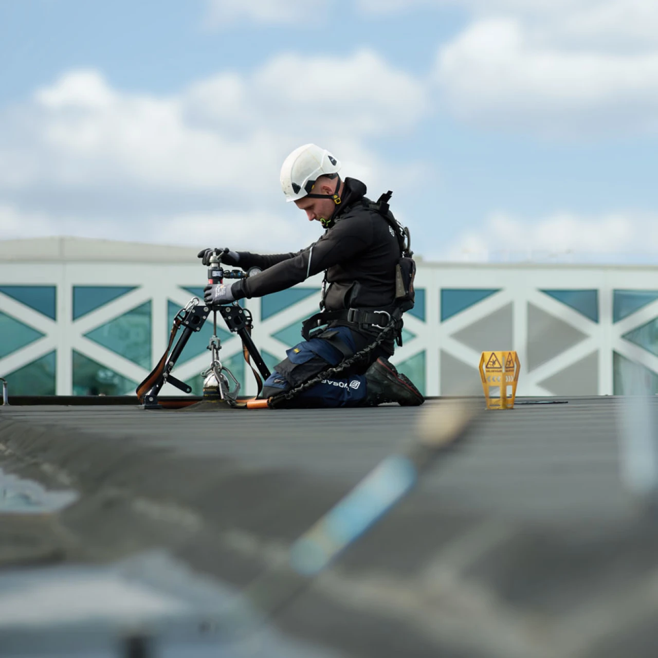 man op plat dak bezig met apparatuur met helm op