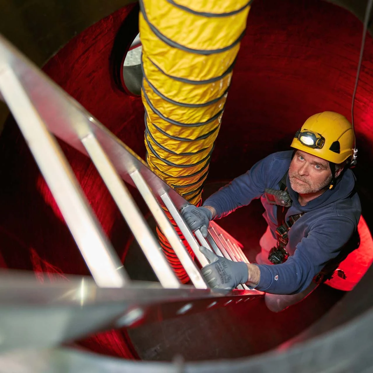 man met helm en lamp op hoofd klimmend op trap in besloten ruimte