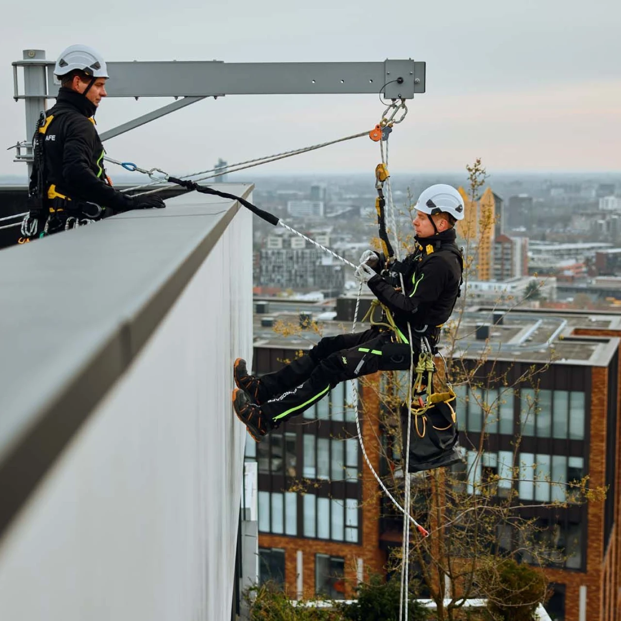 mannen op dak hangend aan touw in harnas met helm op