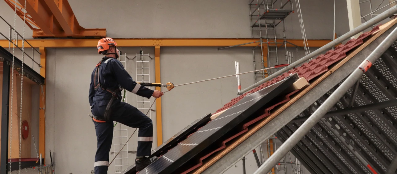 man in loods met helm op en harnas aan lopend op schuin dak