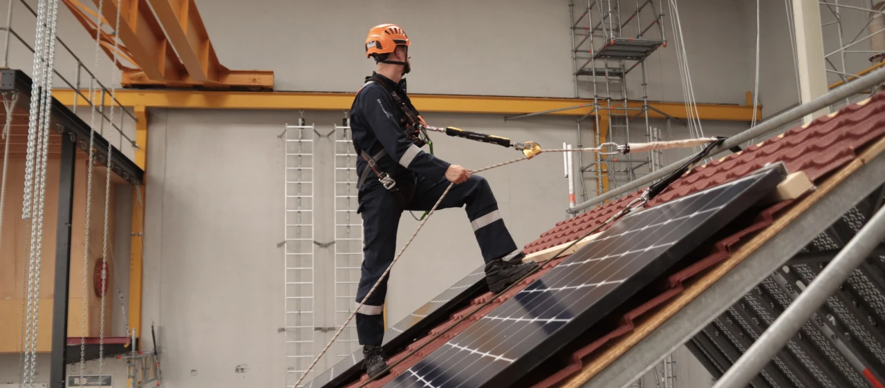 man op dak met touwen en helm op en harnas aan