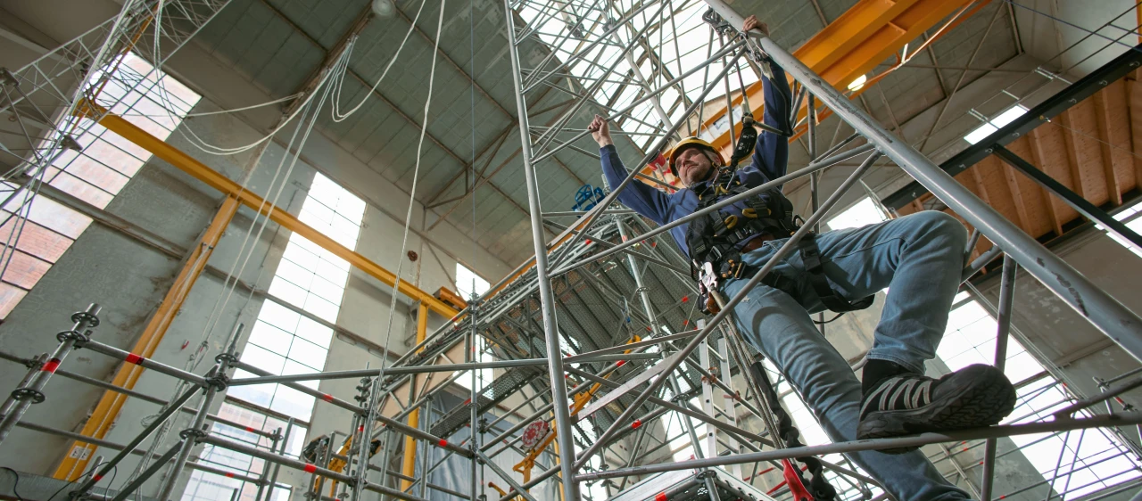 man in harnas en helm op klimmend op ladder in loods