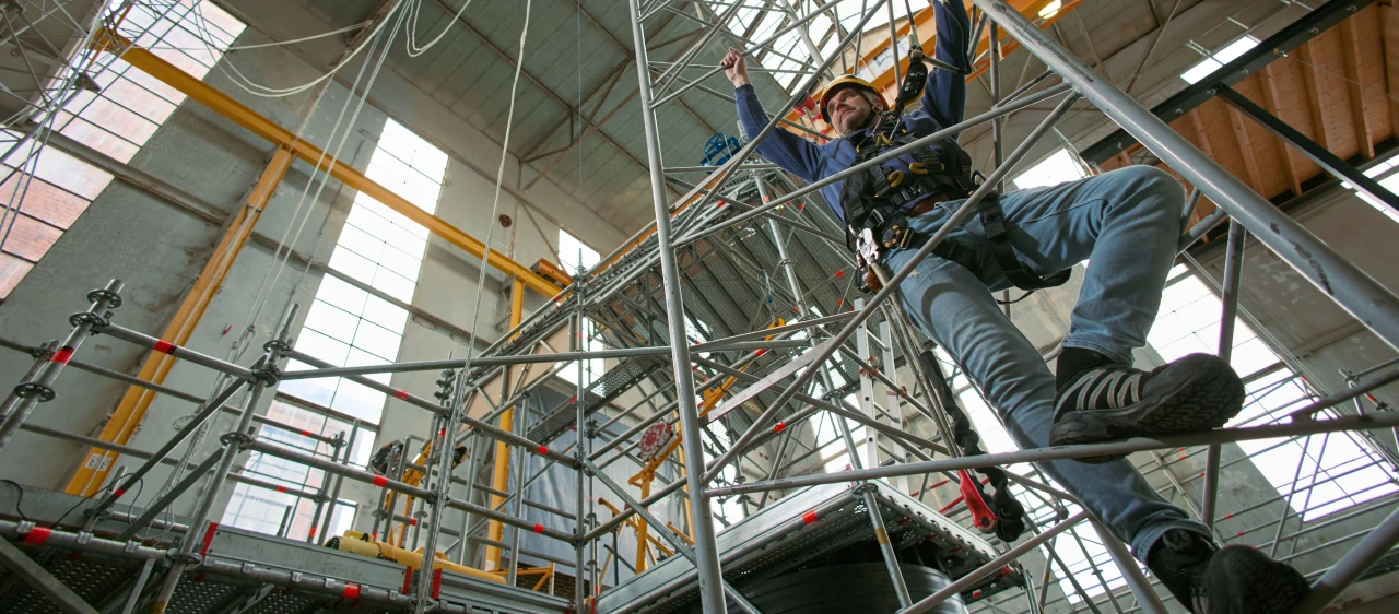man op ladder in loods met harnas en helm