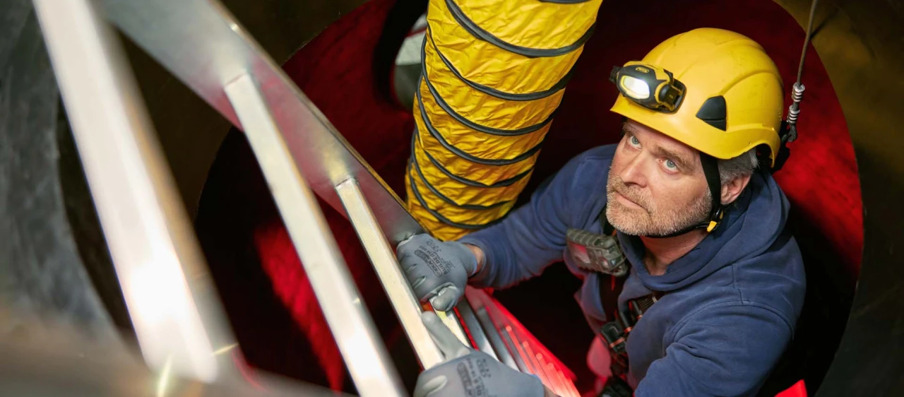 man klimmend op ladder met helm op en harnas aan in besloten ruimte