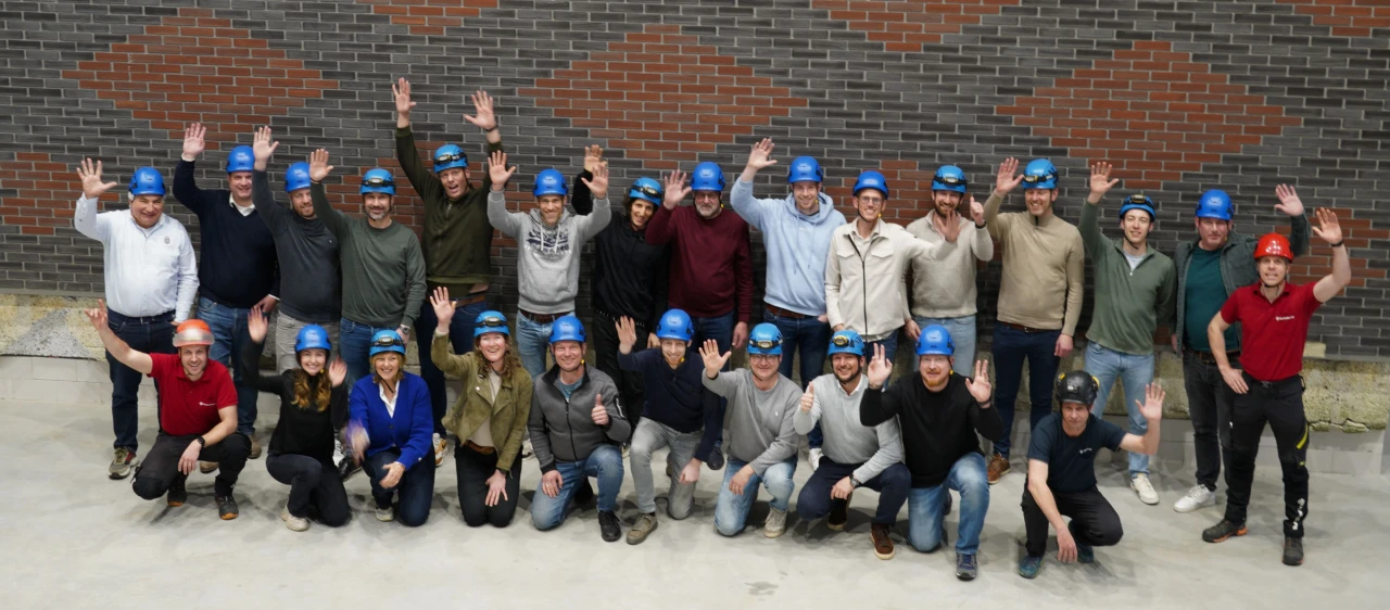 Een groep mensen die voor een huis staan met een blauwe helm