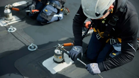 mannen op plat dak met helm op en harnas aan bezig met ankerpunten