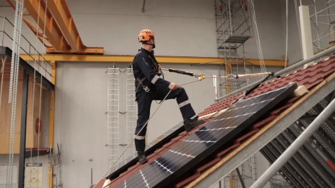 man op dak met touwen en helm op en harnas aan