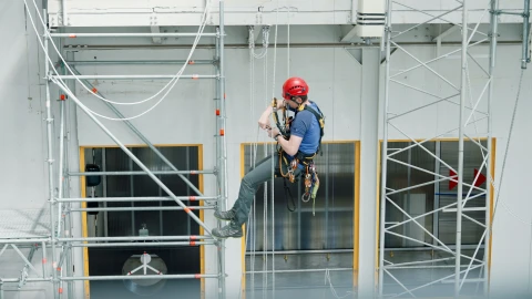 man hangend in touwen op hoogte met helm en harnas