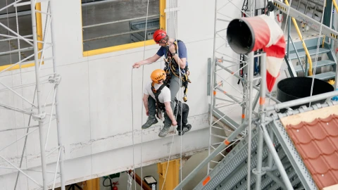 mannen hangend aan touwen op hoogte met harnas en helm