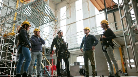 personen in rij in loods met helm en harnas