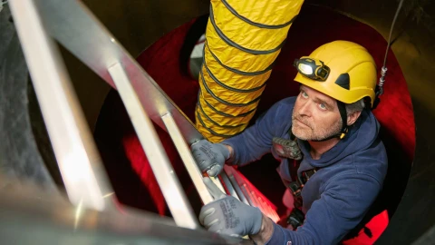 man op trap in besloten ruimte met helm met lamp erop