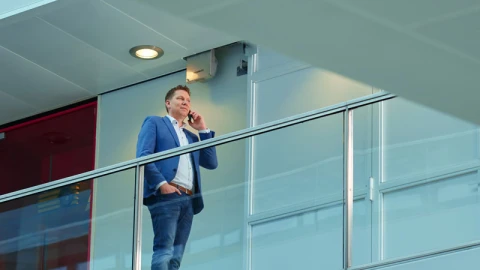 bellende man met pak aan achter glazen leuning