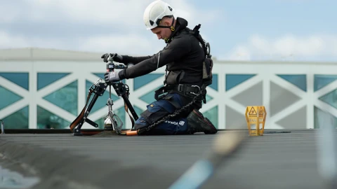 man op plat dak bezig met apparatuur met helm op