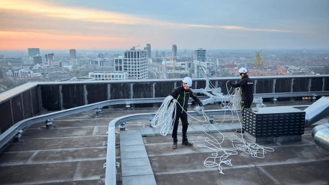 mannen op hoog dak met helm op en touw vast