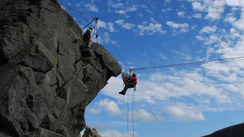 grote rots met man hangend in touw met helm en brancard