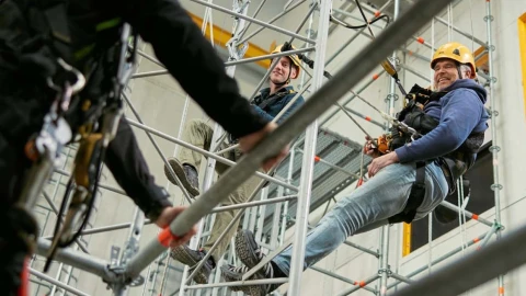 personen op hoogte hangend aan touw met helm op en harnas aan