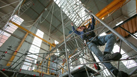 man op trap in loods met harnas en helm