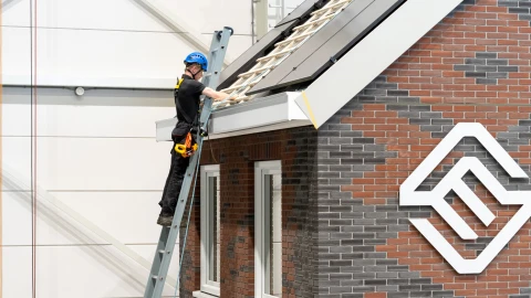 een man die op een ladder staat naast het dak van een woning met zonnepanelen