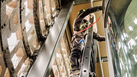een man die staat op een ladder naast een glazen gevel met valbeveiliging aan