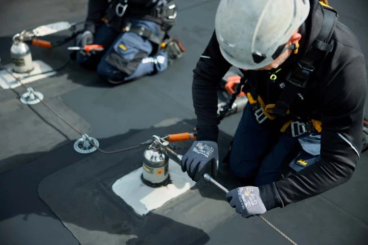 mannen op plat dak met helm op en harnas aan bezig met ankerpunten