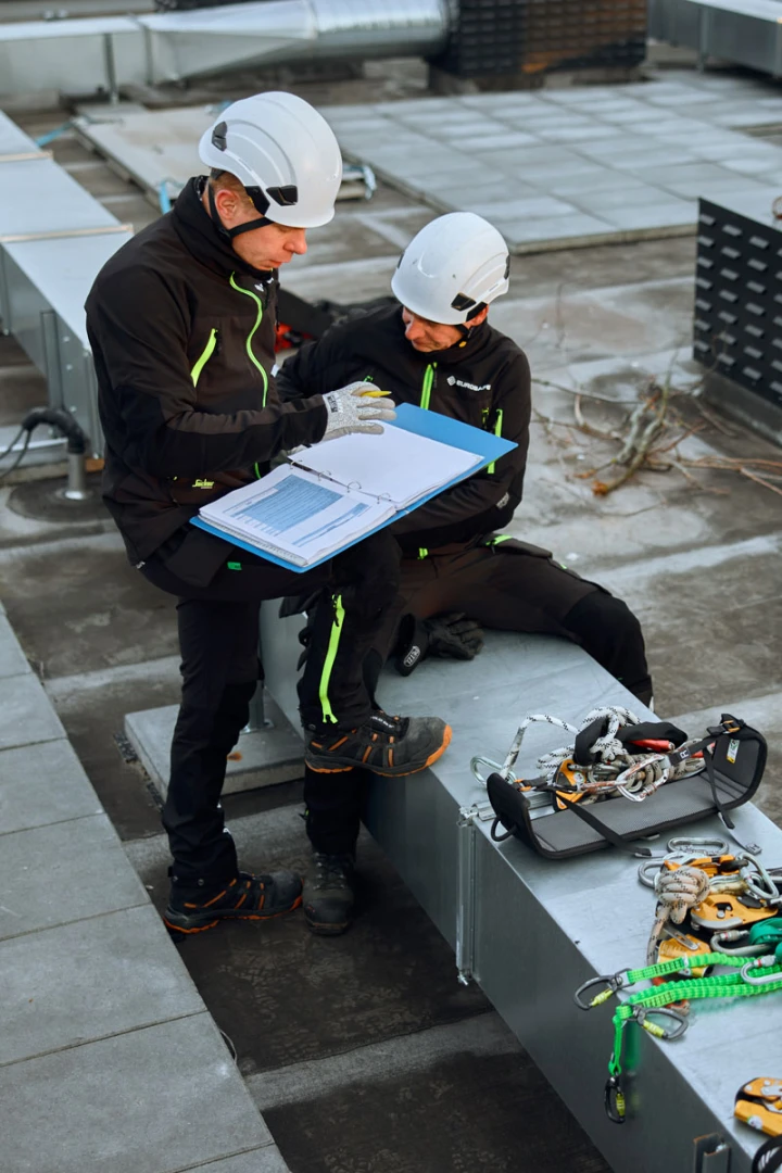 twee mannen met map op dak aan het overleggen