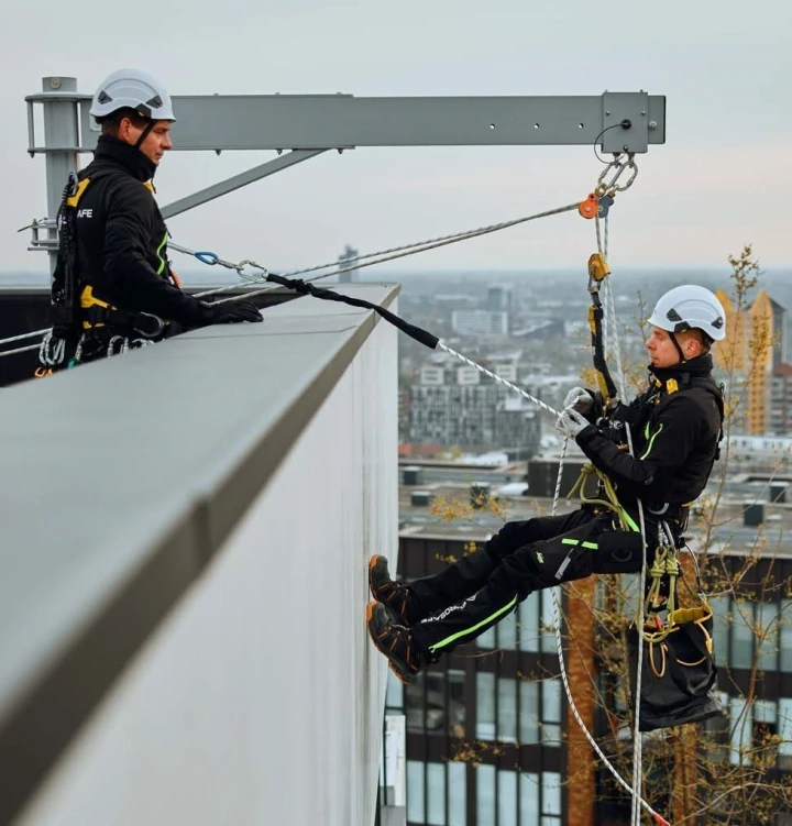 twee mannen op hoog dak met beveiliging man hangt aan dak
