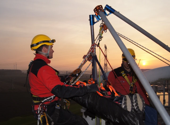 mannen aan touw met helm op in harnas op dak iemand op brancard aan het begeleiden