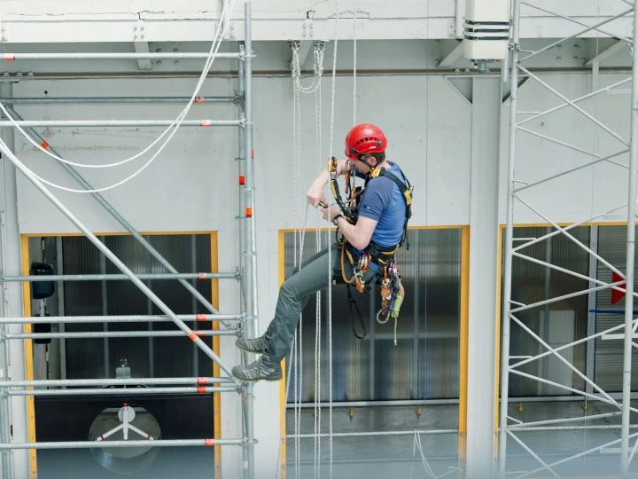 man hangend in touwen op hoogte met helm en harnas