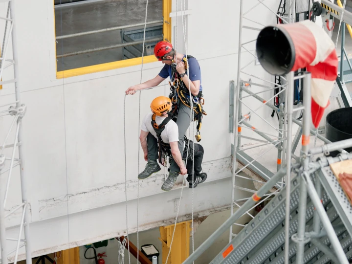 mannen hangend aan touwen op hoogte met harnas en helm