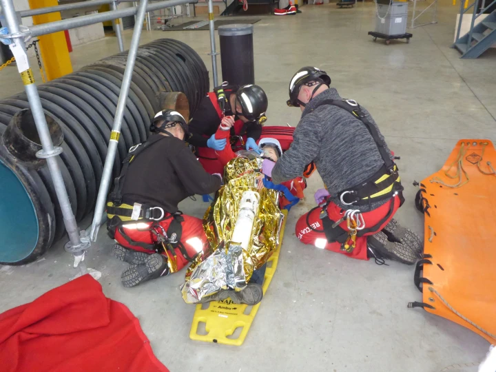 mensen aan het oefenen met redden van persoon op brancard met helm en harnas op